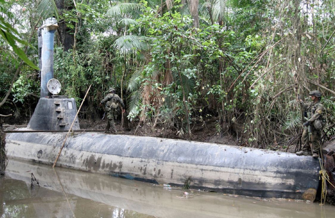 Low-profile semi-submersible vessel photographed near a forested shoreline